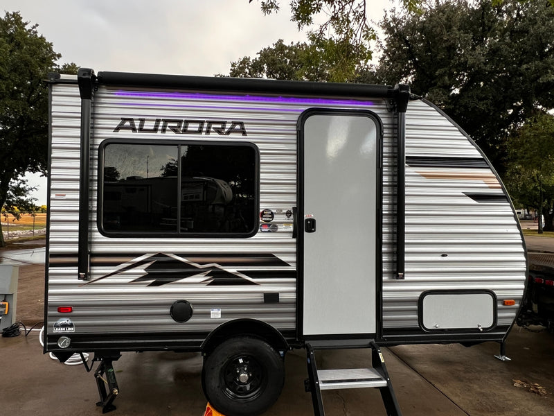 This Aurora travel trailer RV rental, with its illuminated awning and side door, is set up for a comfortable outdoor adventure. — photo 2