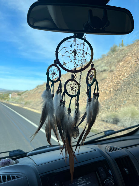 A dreamcatcher with feathers and crystals hangs from the rearview mirror of an RV rental, on a scenic desert road trip.