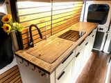 Experience comfort in this RV rental! Its kitchen boasts wooden counters, a built-in cooktop, sink, and wood-paneled walls.