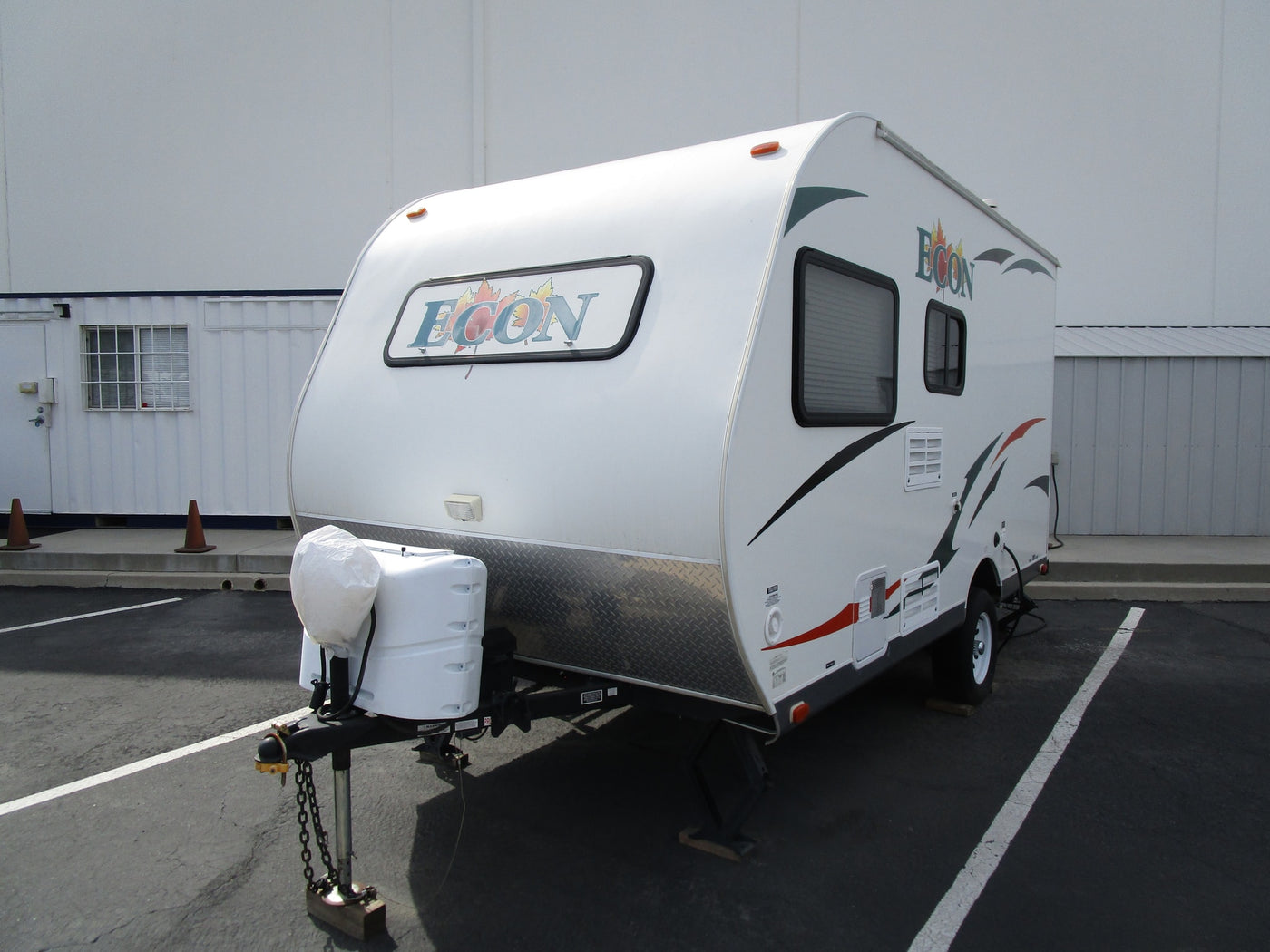 A white ECON travel trailer, suitable for RV rental, is parked on asphalt with a light-colored building in the background. — photo 2