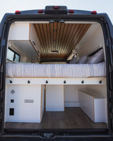Spacious RV rental interior: cozy bed, smart storage, and wood ceiling details. Perfect van conversion for travel.