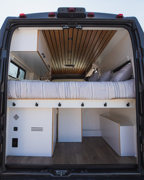 Spacious RV rental interior: cozy bed, smart storage, and wood ceiling details. Perfect van conversion for travel.