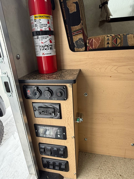 RV rental control panel: electrical outlets, light switches, Xantrex inverter display, and a safety fire extinguisher.