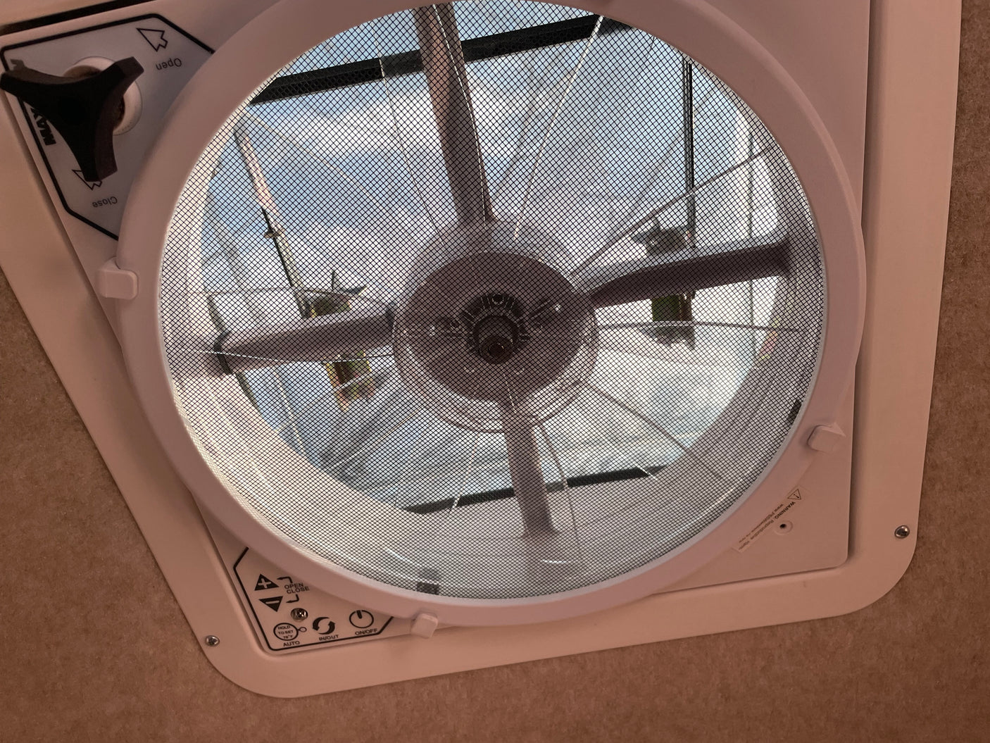 An RV rental ceiling fan with mesh screen and controls. The fan blades are visible through the screen, with sky beyond.