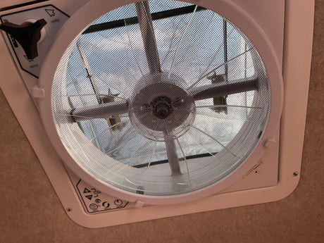 An RV rental ceiling fan with mesh screen and controls. The fan blades are visible through the screen, with sky beyond.