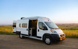Spacious white camper van rv rental with open doors, parked on a dirt road at sunset. Ideal for outdoor adventures.