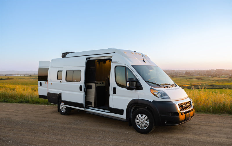  is parked on a dirt road amidst green fields at sunset.|A white RV rental camper van with open rear doors on a dirt road — photo 10
