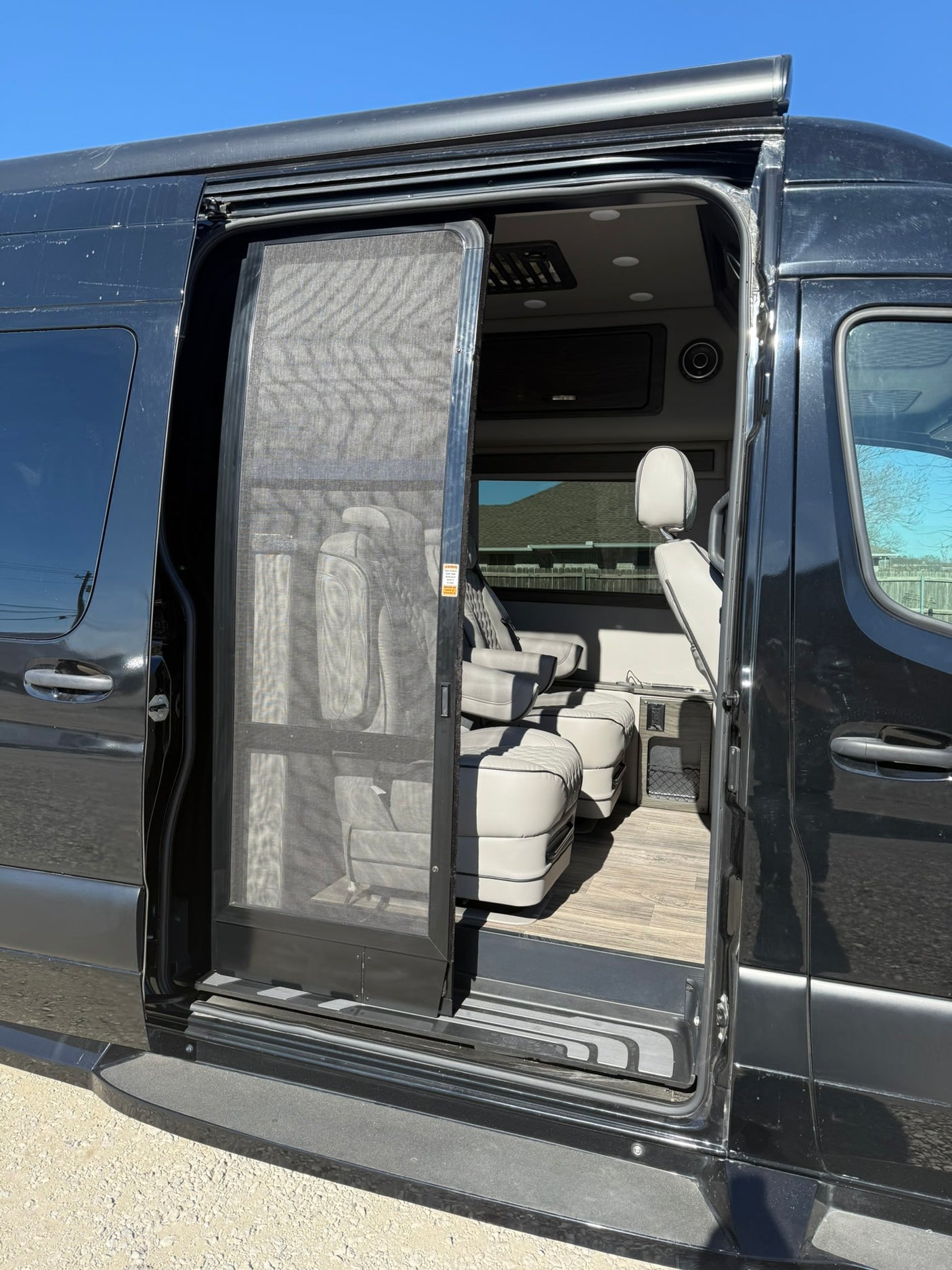 Open side door of a black rv rental van, showing the screen door and plush interior with captain's chairs.