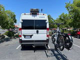 Rear view of a white Winnebago RV rental van, featuring a rooftop AC and two e-bikes on a hitch-mounted rack.