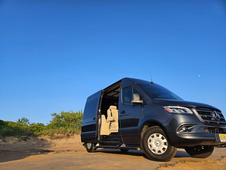 Experience premium travel with our luxury Mercedes-Benz Sprinter RV rental, featuring an open side door revealing a plush interior on a sandy road.