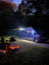 Cozy night camping with an RV rental: warm campfire, chairs, and an illuminated camper setup under the trees.