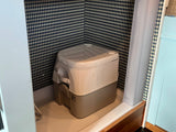 Inside an RV rental: a portable toilet sits in a small, patterned nook with blue geometric wallpaper and a shower curtain.