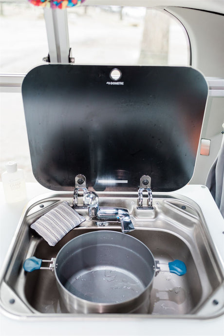 Close-up of an RV rental's compact kitchen sink, featuring a Dometic cover, pot, and sponge. Ideal for small spaces.