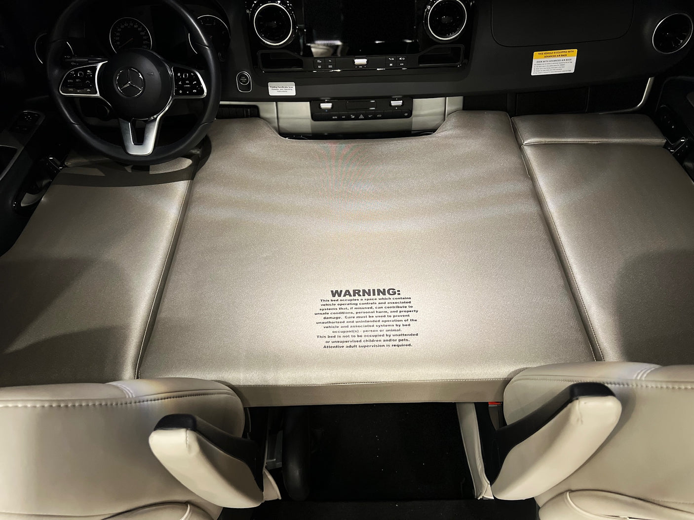 An rv rental's cockpit transforms into a temporary bed with a warning about vehicle controls & supervision.