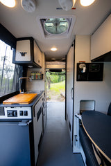 Inside a modern rv rental: full kitchen, dining nook, bunk bed, and view to nature. Bright, clean, and adventure-ready van interior.