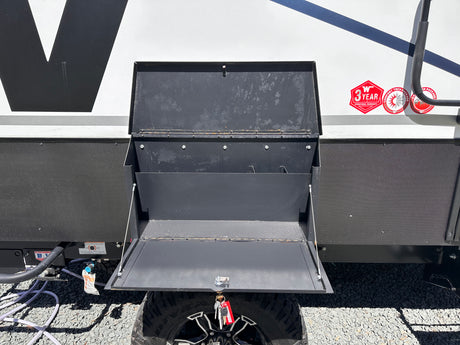 Open black metal storage compartment on an RV, revealing inner shelves, utility hookups, and a tire. Useful for RV rental setup.