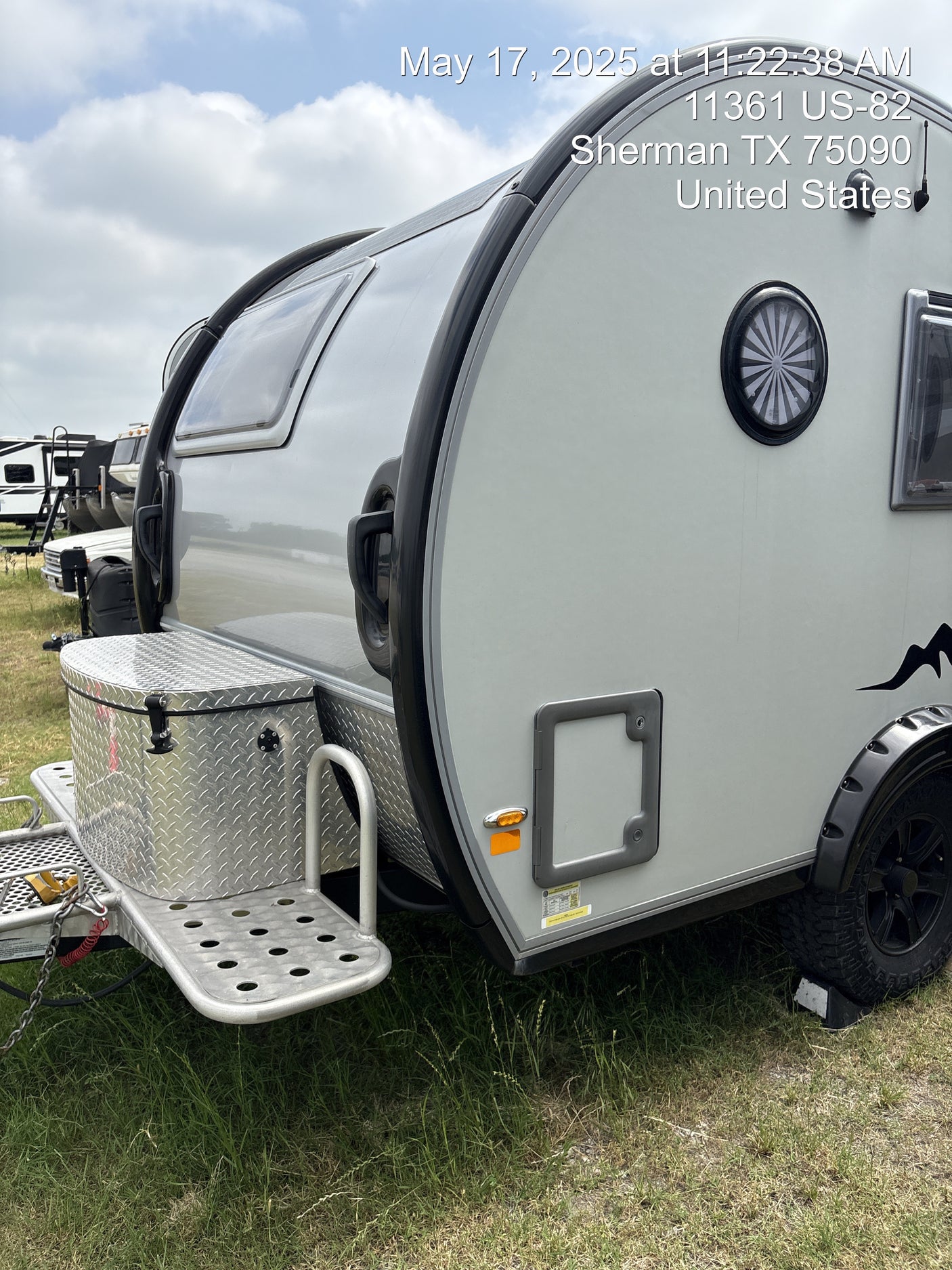 A modern teardrop camper, perfect for an RV rental adventure, parked on grass at a campsite.
