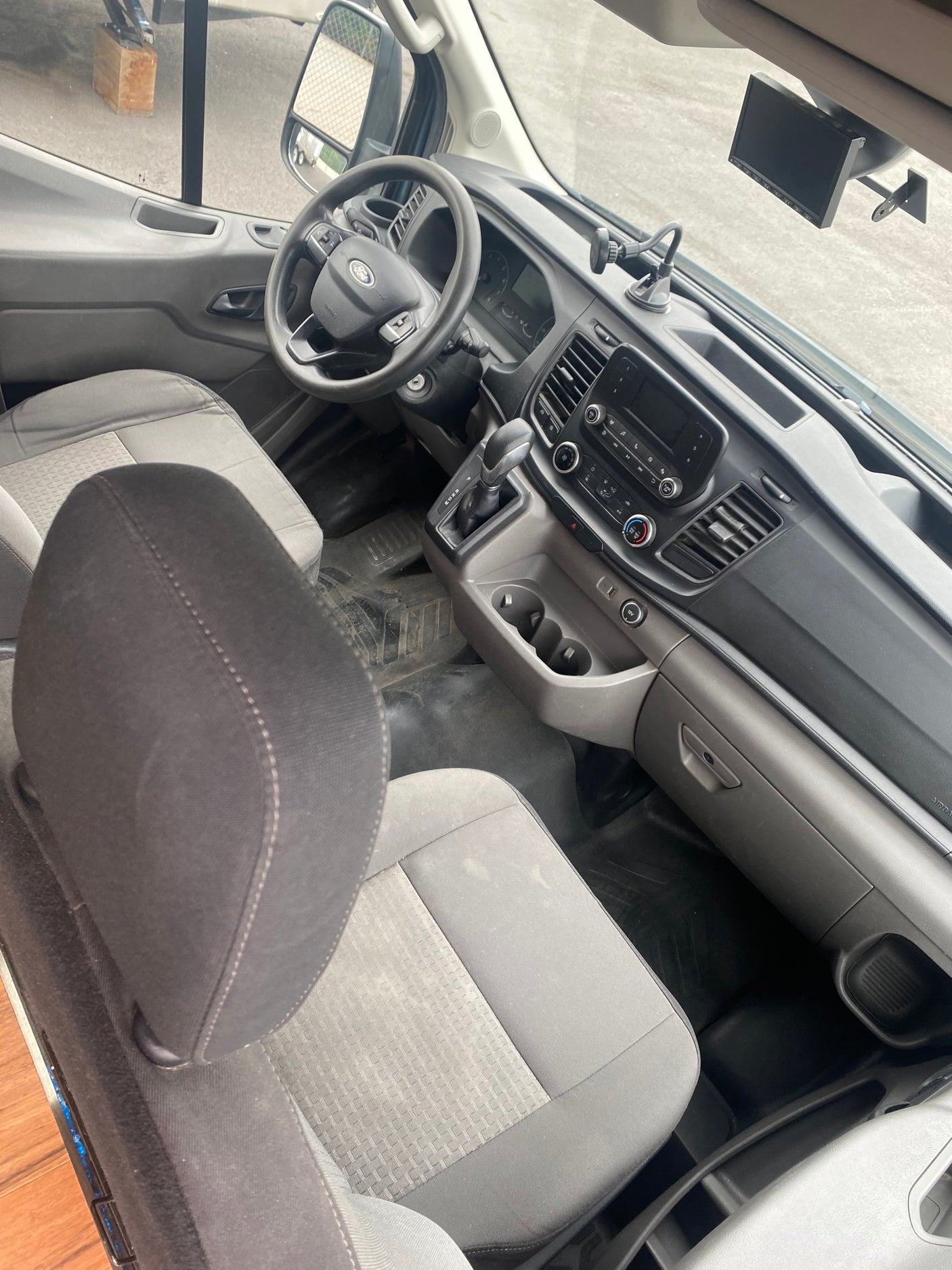 RV rental van cockpit: driver's area with gray seats, Ford steering wheel, dash, screen, gear shifter & cup holders.