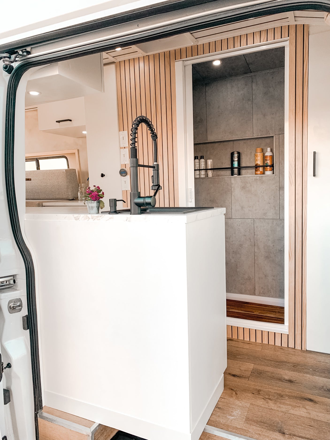 Stylish RV rental interior: view from open door showing a modern kitchen sink and a tiled shower stall with wooden floor.
