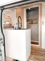 Stylish RV rental interior: view from open door showing a modern kitchen sink and a tiled shower stall with wooden floor.
