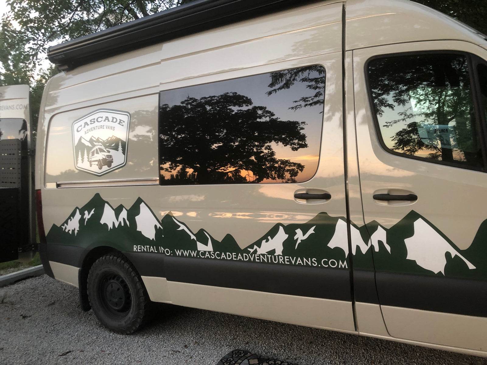 Customized adventure van for RV rental, featuring a mountain decal & sunset reflected in the window.