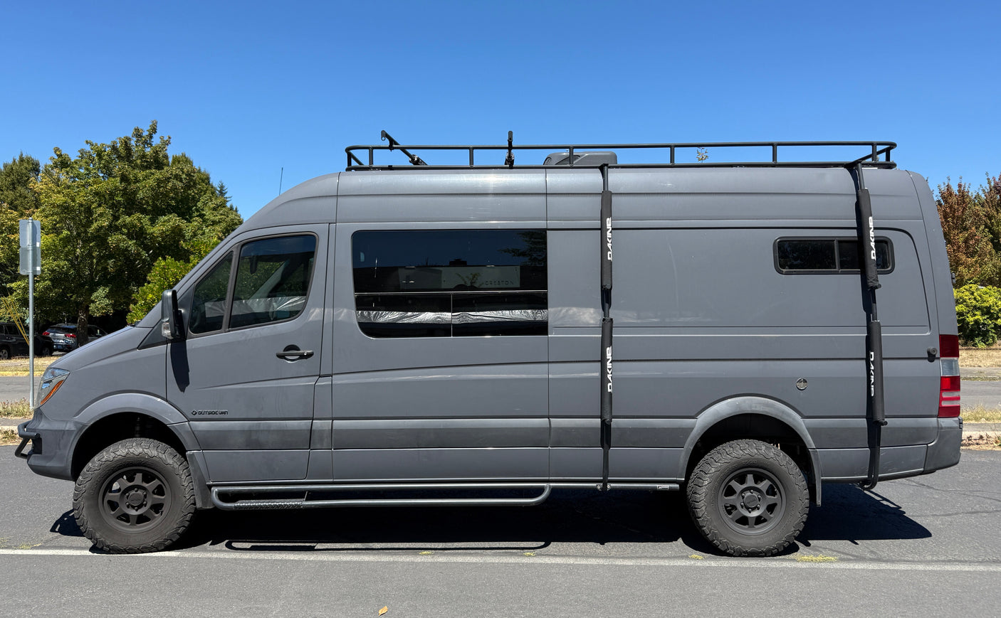 Side view of a rugged gray Mercedes Sprinter adventure van with off-road tires and roof rack, perfect for an RV rental.