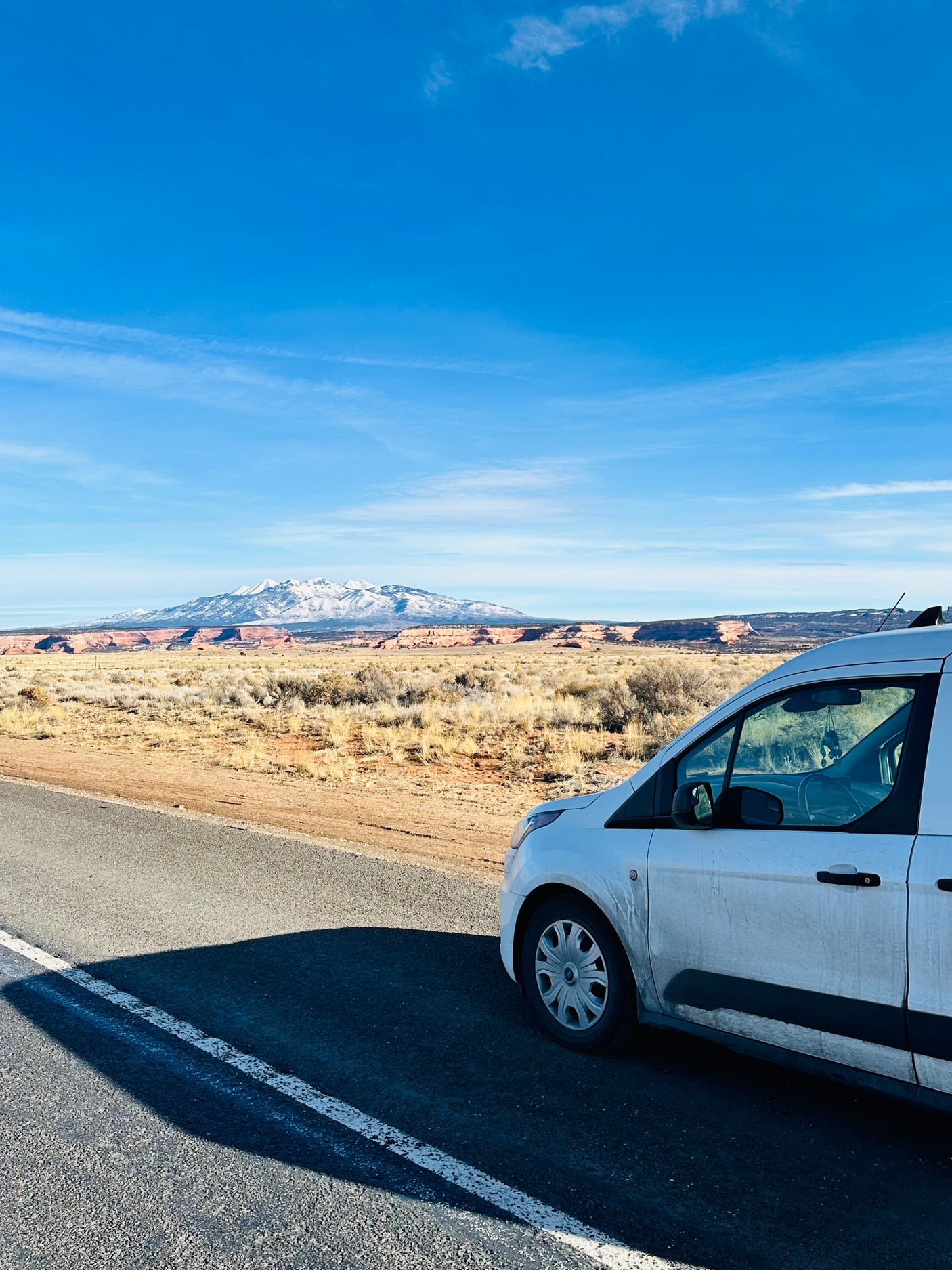 White RV rental van stopped on a road, overlooking a desert landscape with distant snow-capped mountains.