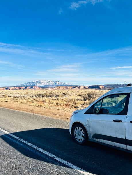 White RV rental van stopped on a road, overlooking a desert landscape with distant snow-capped mountains.