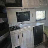 Inside an RV rental: well-equipped kitchen with stove, sink, microwave, fridge, and AC unit.