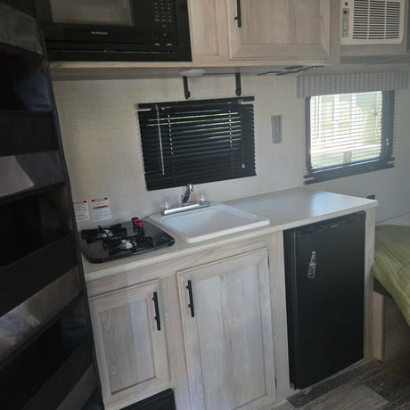 Inside an RV rental: well-equipped kitchen with stove, sink, microwave, fridge, and AC unit.
