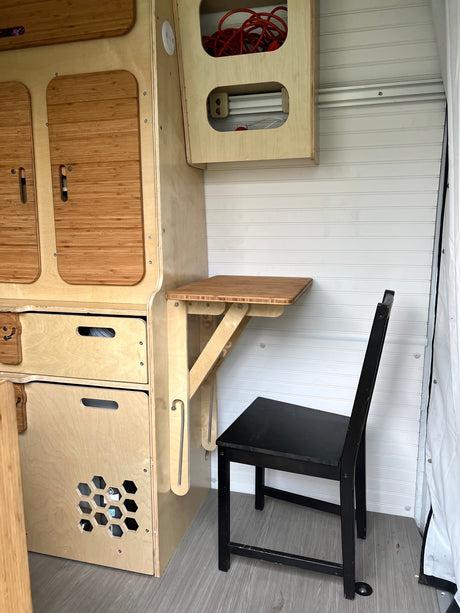 Inside this RV rental: custom wood storage, drawers, and a bamboo fold-down table with a chair, designed for compact living.