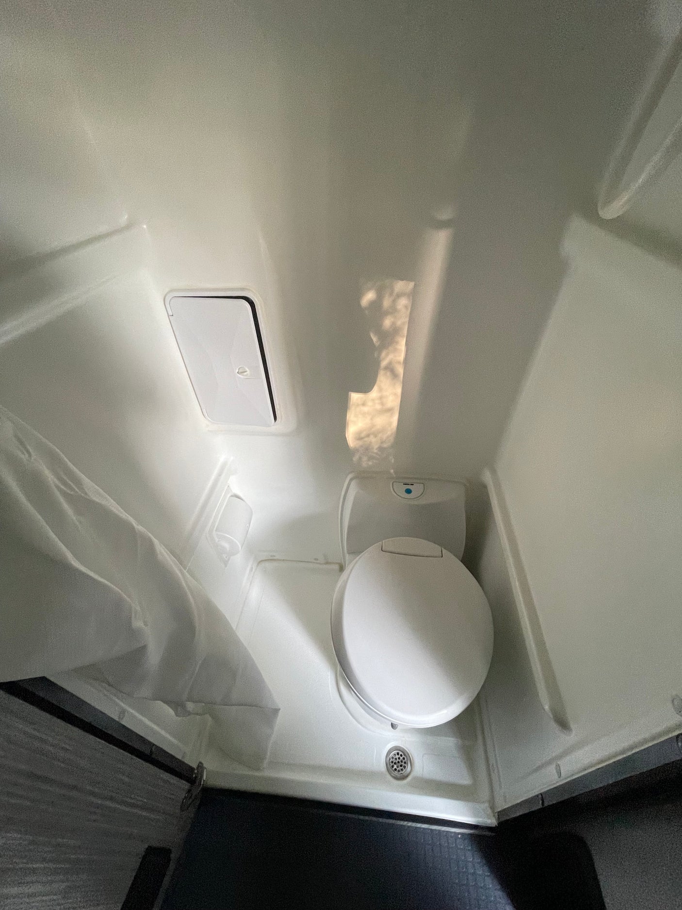 Compact RV rental bathroom with a toilet, shower curtain, and floor drain.