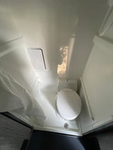 Compact RV rental bathroom with a toilet, shower curtain, and floor drain.