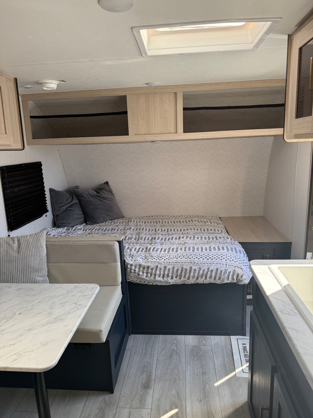 Modern RV rental interior with a cozy bed, dinette, overhead storage, and kitchen counter. Bright and functional for travel. — photo 4