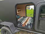 View into a dark grey teardrop camper's open door, showing a cozy bed and shelf. Great for an rv rental adventure.