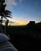 Inside our RV rental, an open door frames a calming ocean sunset. Palm trees and the moon complete this perfect travel view.