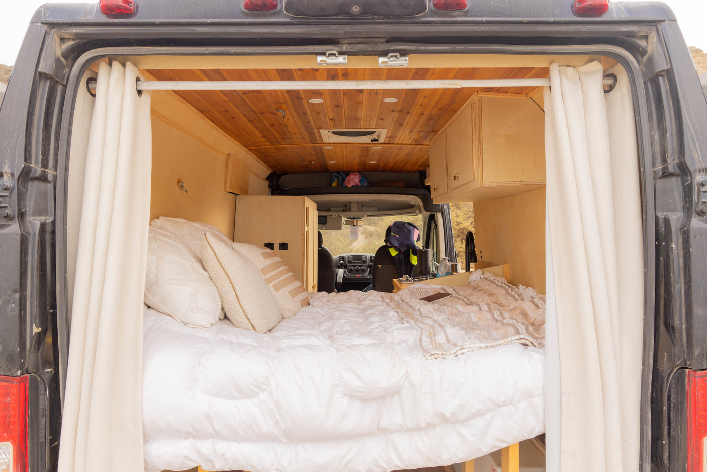 Cozy rv rental van interior from the back, featuring a comfortable bed, wooden walls, and a compact kitchen area.
