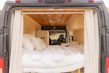 Cozy rv rental van interior from the back, featuring a comfortable bed, wooden walls, and a compact kitchen area.