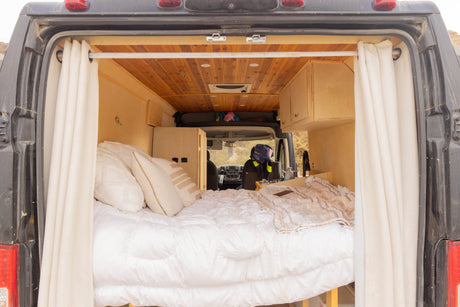Cozy rv rental van interior from the back, featuring a comfortable bed, wooden walls, and a compact kitchen area.