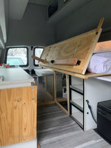 Lifted bed reveals storage in this camper van rv rental interior, with a compact kitchen and fridge for road trips.