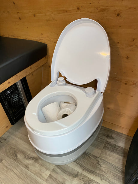 Clean portable toilet with toilet paper in an **rv rental** interior, featuring wood walls and floor.