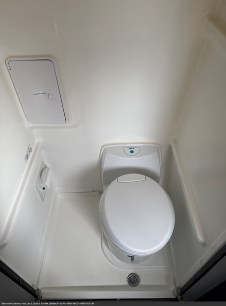 This clean RV rental bathroom features a Thetford toilet, overhead toilet paper storage, and a shower drain for convenience.