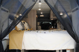 RV rental interior: A cozy bedroom with patterned pillows, white bedding, and mesh bug screens for comfortable travel.