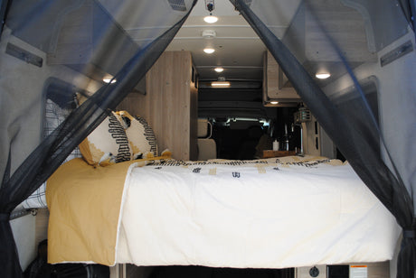 RV rental interior: A cozy bedroom with patterned pillows, white bedding, and mesh bug screens for comfortable travel.