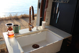 Interior of an RV rental kitchen with a large white sink, rose gold faucet, coffee setup, and ocean view.