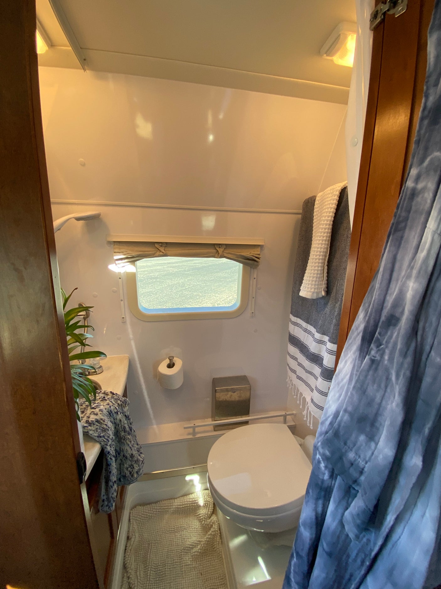 Cozy RV rental bathroom with toilet, shower, sink, window, and towels, perfect for compact travel trailer comfort.