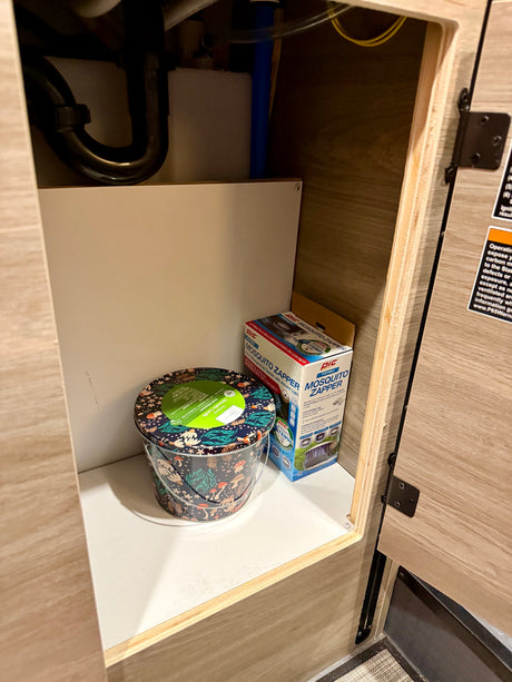 RV rental under-sink storage with a PIC Mosquito Zapper, citronella candle, and plumbing visible, essential for camping comfort.