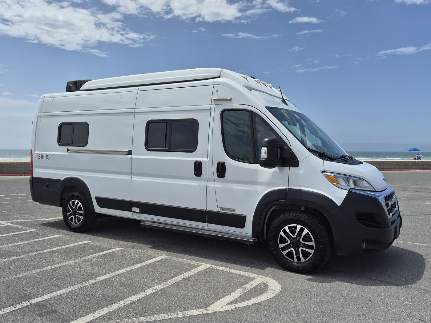  showcasing its rear and side with a Florida license plate under a blue sky.|A white Winnebago Solis camper van rv rental is parked in a sunny coastal lot — photo 10
