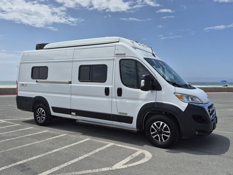  showcasing its rear and side with a Florida license plate under a blue sky.|A white Winnebago Solis camper van rv rental is parked in a sunny coastal lot — photo 10