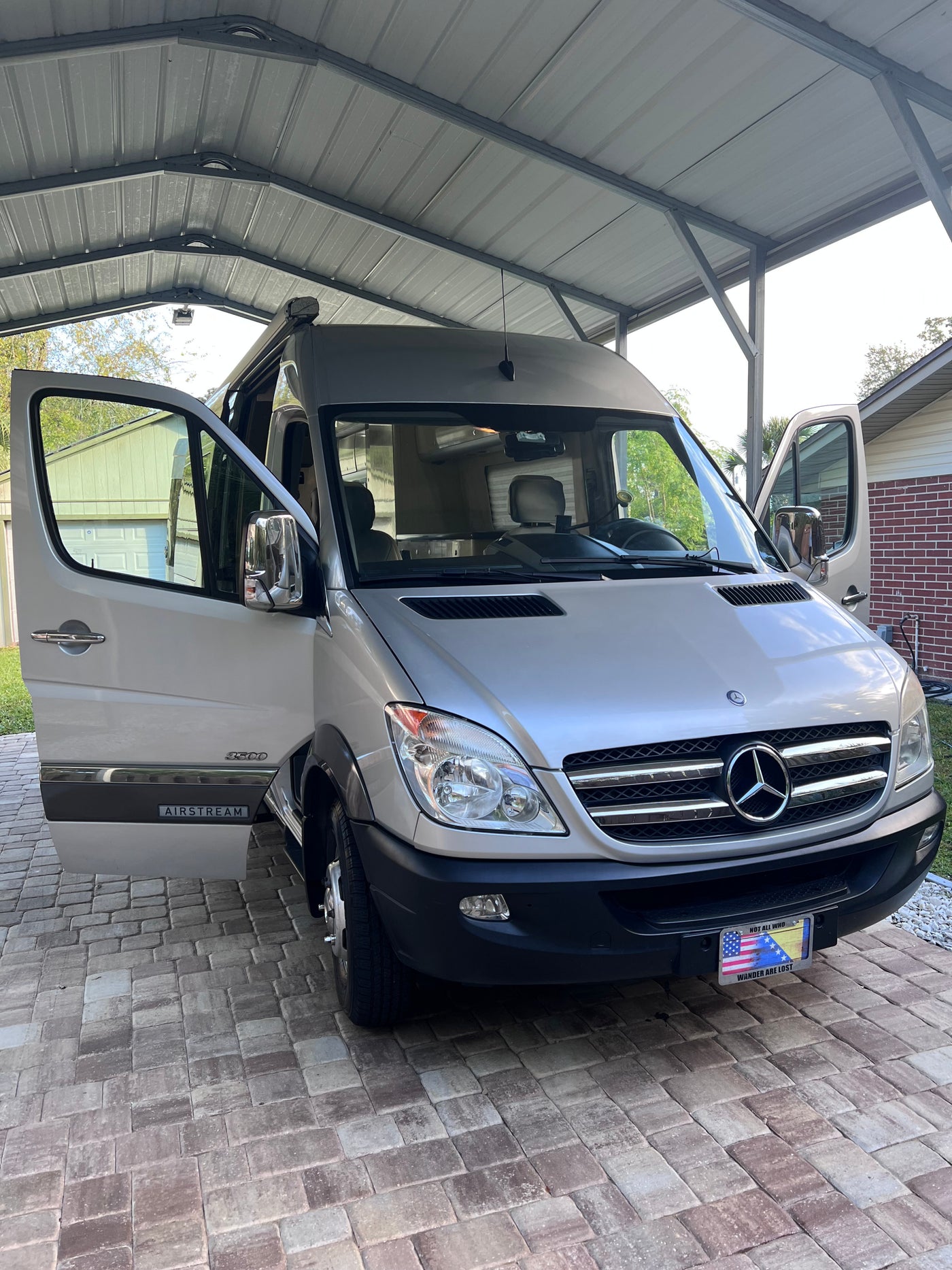 Silver Airstream Mercedes Sprinter RV rental camper van parked under a carport with doors open on pavers.